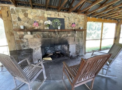 A rustic stone fireplace with wooden chairs arranged around it, decorated with flowers and small American flags.