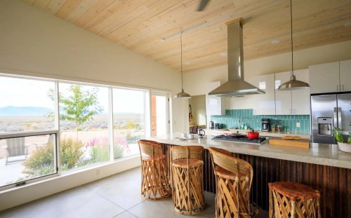 Modern kitchen with a large island, bar stools, and large windows showcasing a scenic view. Bright and airy design.