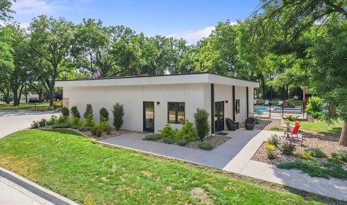 Modern building surrounded by greenery, featuring a landscaped yard and outdoor seating area.