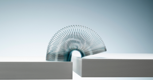 A metal spring toy arches gracefully between two white surfaces, creating a dynamic visual contrast.