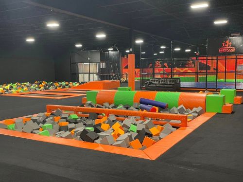 Indoor trampoline park featuring foam pits, colorful obstacles, and a lounge area with a couch.