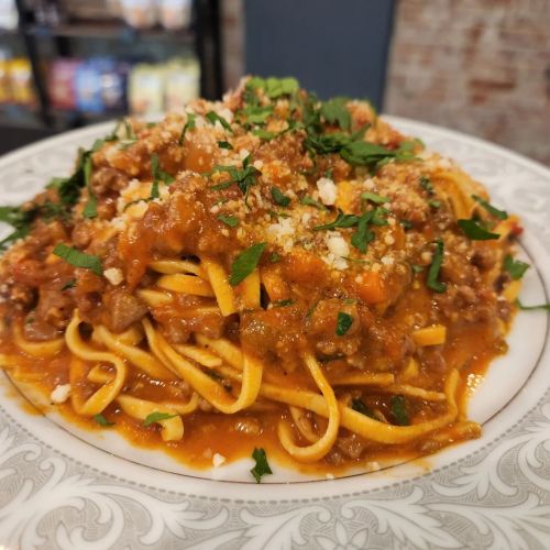 A plate of linguine topped with a rich meat sauce, garnished with herbs and grated cheese.