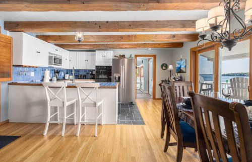 Bright kitchen with wooden beams, white cabinets, and a dining area featuring a large table and chairs, overlooking a lake.