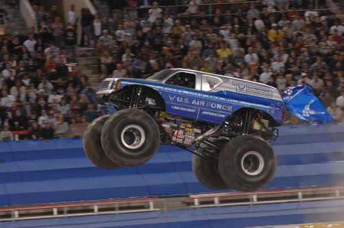 A monster truck with U.S. Air Force branding jumps over a ramp in front of a cheering crowd at a stadium event.