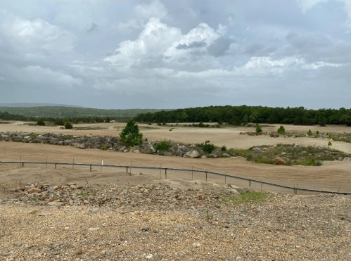 A barren landscape with rocky terrain, sparse vegetation, and a cloudy sky in the background.