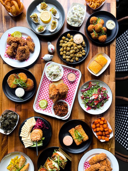 A vibrant spread of Southern dishes, including fried chicken, collard greens, salads, and various appetizers on wooden table.
