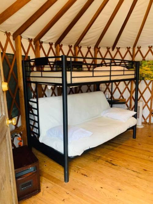 A cozy yurt interior featuring a black bunk bed with a futon below, wooden floors, and a rustic wooden door.