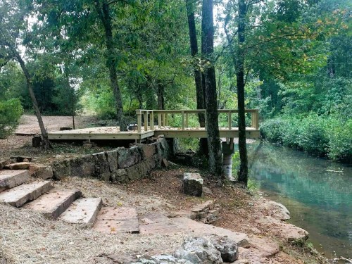 A wooden platform by a serene creek, surrounded by trees and rocky steps leading to the water.