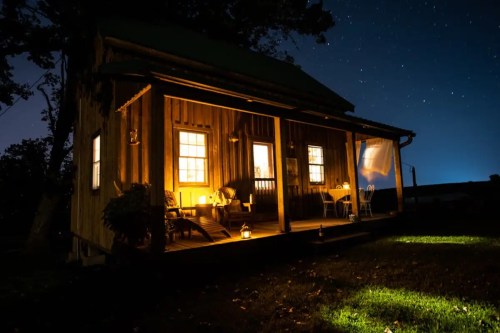 A cozy wooden cabin illuminated at night, surrounded by stars and a peaceful outdoor setting.