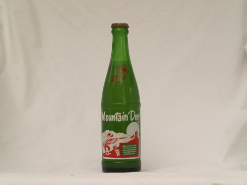 A vintage green glass bottle of Mountain Dew with a red label and a cork stopper, set against a white background.