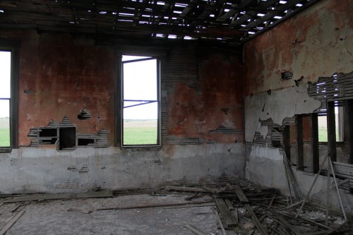 Interior of a dilapidated building with peeling paint, broken windows, and scattered debris on the floor.