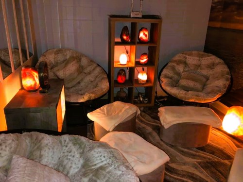 Cozy relaxation space with plush chairs, soft ottomans, and glowing salt lamps on shelves, creating a warm ambiance.