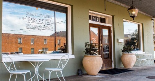 Exterior of Pearl Street Pasta & Wine, featuring a green facade, large windows, and outdoor seating with potted plants.
