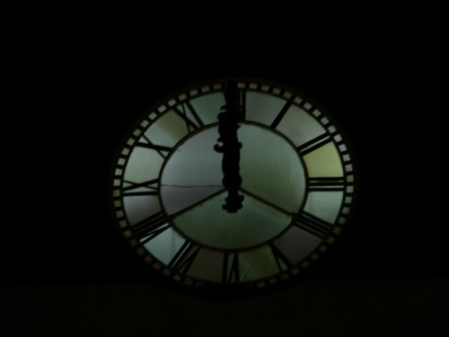 A close-up of a vintage clock face with Roman numerals, illuminated against a dark background.