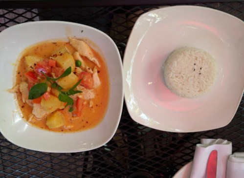 A bowl of chicken curry with vegetables and pineapple, served with a side of white rice on a black table.