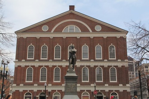Statue in front of a historic brick building with large windows and a cloudy sky.
