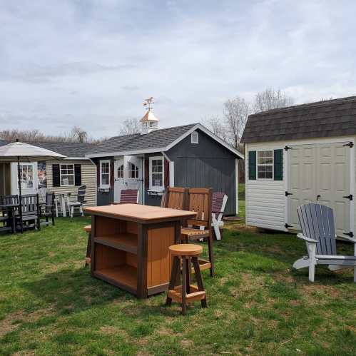 A display of outdoor furniture and storage sheds on a grassy area under a cloudy sky.