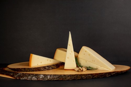 A wooden platter displays various wedges of cheese, including a triangular piece, against a dark background.