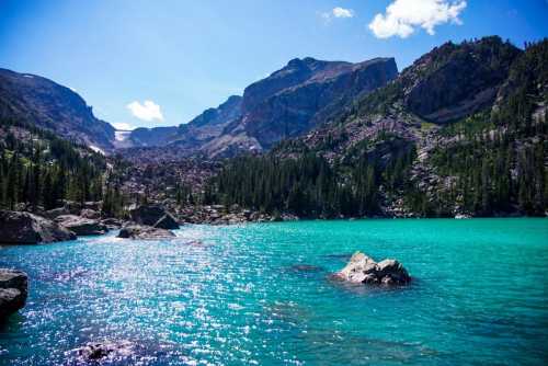 A serene turquoise lake surrounded by mountains and lush greenery under a clear blue sky.