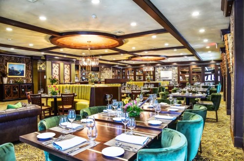Elegant restaurant interior featuring green chairs, wooden tables, and decorative lighting, creating a warm ambiance.