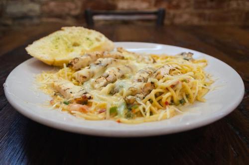 A plate of creamy pasta topped with grilled chicken and cheese, served with a slice of garlic bread.