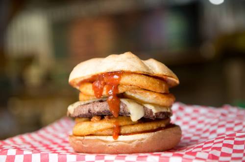 A stacked burger with two patties, cheese, onion rings, and sauce, served on a checkered paper.