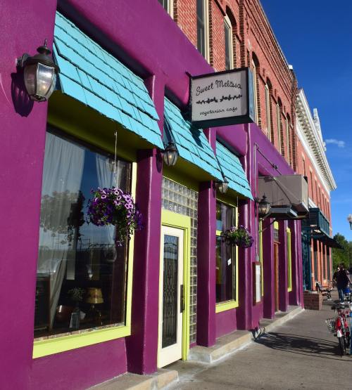 Colorful exterior of Sweet Melissa, a vegetarian café, featuring purple walls and teal awnings with flower baskets.