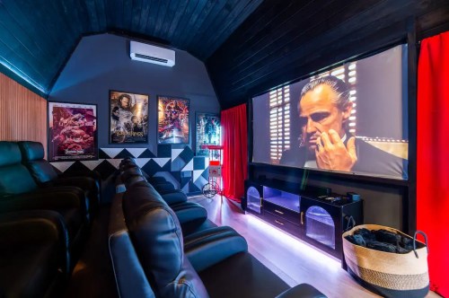A cozy home theater with black recliner seats, a large screen displaying a film, and movie posters on the walls.