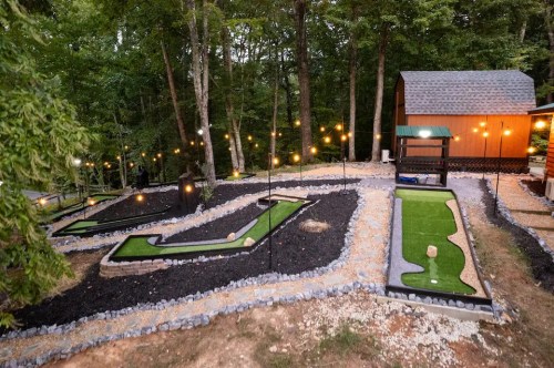A mini-golf course with two holes, surrounded by trees and decorative lights, near a small cabin.