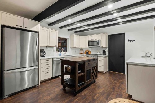 Modern kitchen with white cabinets, stainless steel appliances, a central island, and dark wooden beams on the ceiling.
