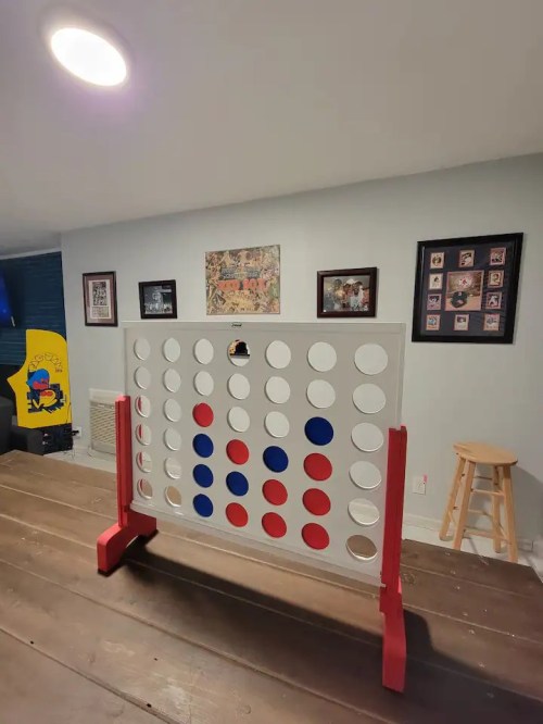 A large Connect Four game on a wooden table, with red and blue discs arranged on a white grid in a cozy room.