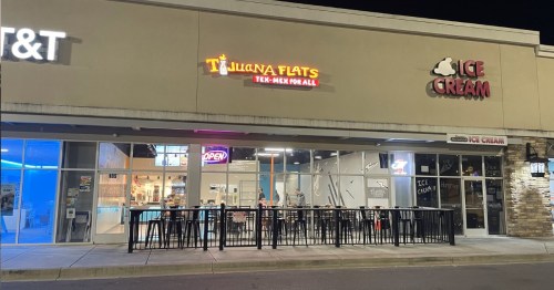 Exterior view of a restaurant and ice cream shop at night, featuring bright signs and outdoor seating.