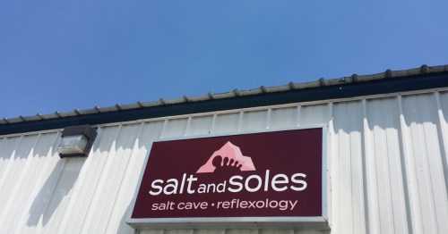 Sign for "Salt and Soles" featuring a salt cave and reflexology services against a clear blue sky.