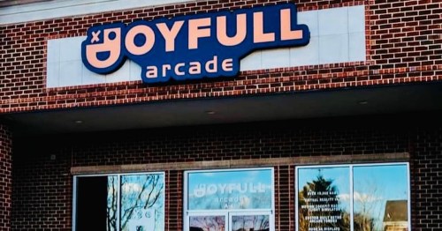 Sign for "Joyfull Arcade" on a brick building, featuring a playful logo and large windows.