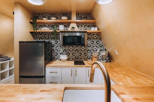 Modern kitchen with wooden countertops, patterned backsplash, stainless steel fridge, and microwave on open shelves.