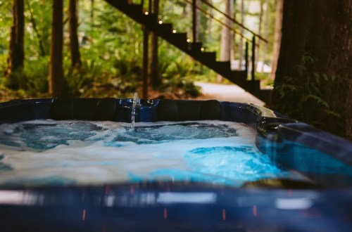 A bubbling hot tub surrounded by lush greenery and a wooden staircase in a serene forest setting.