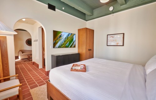 A cozy bedroom with a white bed, wooden furniture, and a TV, featuring warm tones and a welcoming atmosphere.