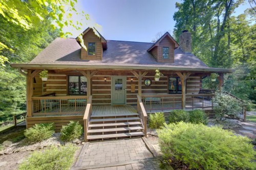 A charming log cabin surrounded by trees, featuring a front porch and landscaped garden.