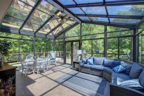 Bright sunroom with glass walls, featuring a cozy sectional sofa, dining table, and views of greenery outside.