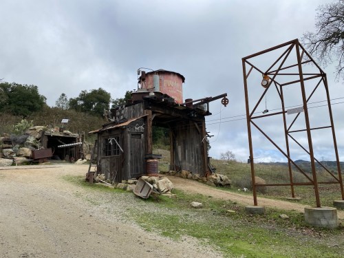 A rustic mining structure with a metal tank on top, surrounded by rocky terrain and a tall metal framework.