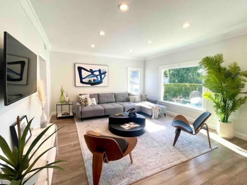 Bright living room with a gray sofa, round coffee table, plants, and large windows letting in natural light.