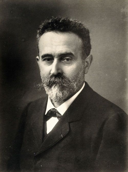 Black and white portrait of a man with a beard, wearing a suit and tie, looking directly at the camera.