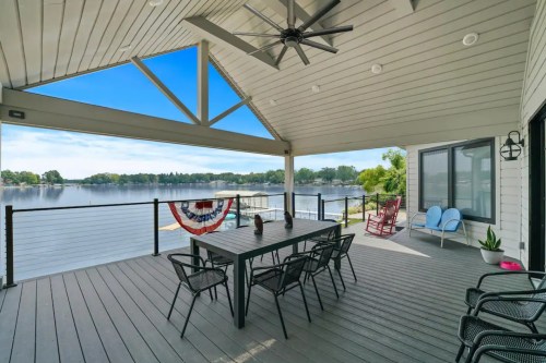 A spacious lakeside patio with a dining table, chairs, and a view of the water under a bright blue sky.