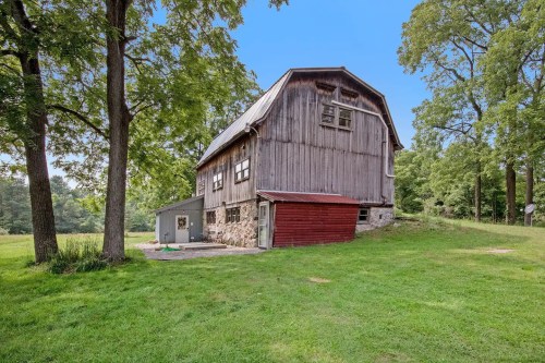 A rustic barn with a red accent, surrounded by lush green trees and grass under a clear blue sky.