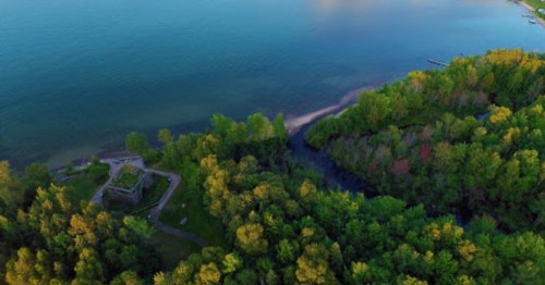 Aerial view of a lush green landscape meeting a calm blue lake, with a small structure near the water's edge.