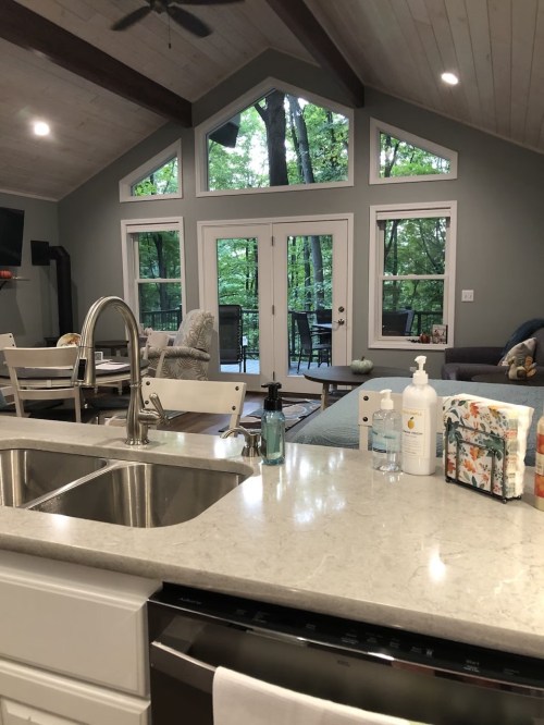 A modern kitchen with a view of a wooded area through large windows, featuring a sink and dining table.