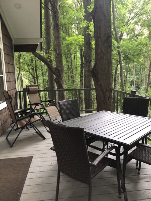 A cozy outdoor deck with a table and chairs, surrounded by lush green trees.