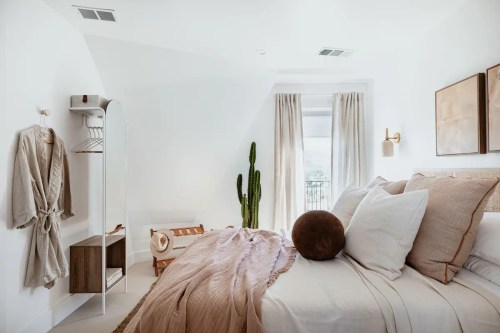Cozy bedroom with a bed, neutral decor, a cactus, and natural light from a window.