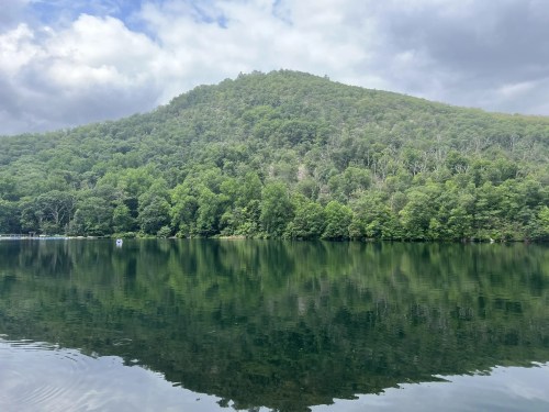 A serene lake reflecting a lush green hillside under a cloudy sky.
