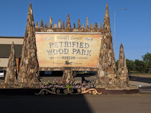 Sign for the World's Largest Petrified Wood Park Museum, featuring a rustic design and surrounded by flowers.